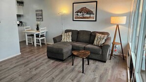 A living room with a gray sectional sofa, a small wooden table, and a dining area with a white table and chairs. - WindanSea Ocean View (San Diego)