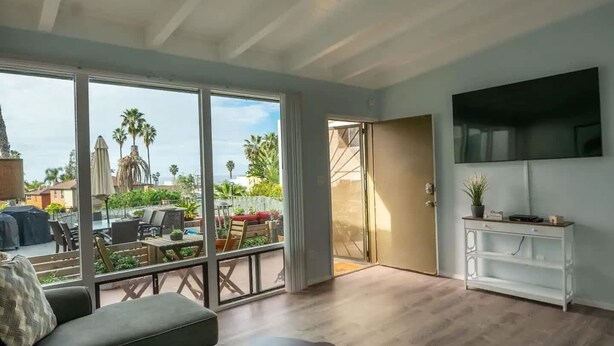 A spacious living area with a large sliding glass door leading to an outdoor patio, a flat-screen TV mounted on the wall, and a white console table. - WindanSea Ocean View (San Diego)
