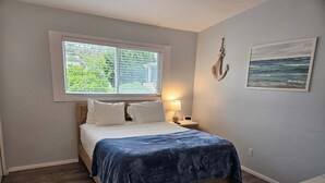 A bedroom with a wooden bed, a window with blinds, a nightstand with a lamp, and a painting on the wall. - WindanSea Ocean View (San Diego)