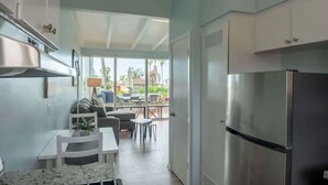 A compact kitchen with a refrigerator, a dining table with chairs, and a view of the outdoors through large windows. - WindanSea Ocean View (San Diego)