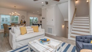 A spacious living room with a white sofa, a blue armchair, a wooden coffee table, and a staircase leading to an upper level.