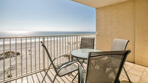 Ein Balkon mit einem Glastisch und zwei Stühlen, mit Blick auf einen Strand und freiem Blick auf das Meer.