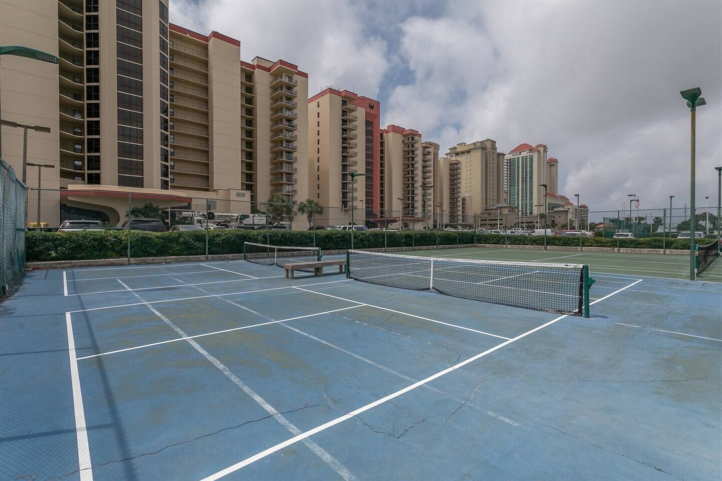 An outdoor tennis court with a net, surrounded by a fence and benches.