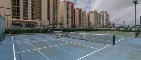 An outdoor tennis court with a net, surrounded by a fence and benches.