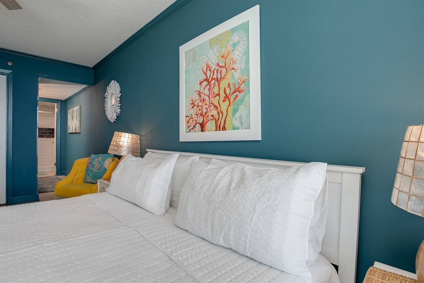 A bedroom with teal walls, a white bed, and a colorful abstract painting.