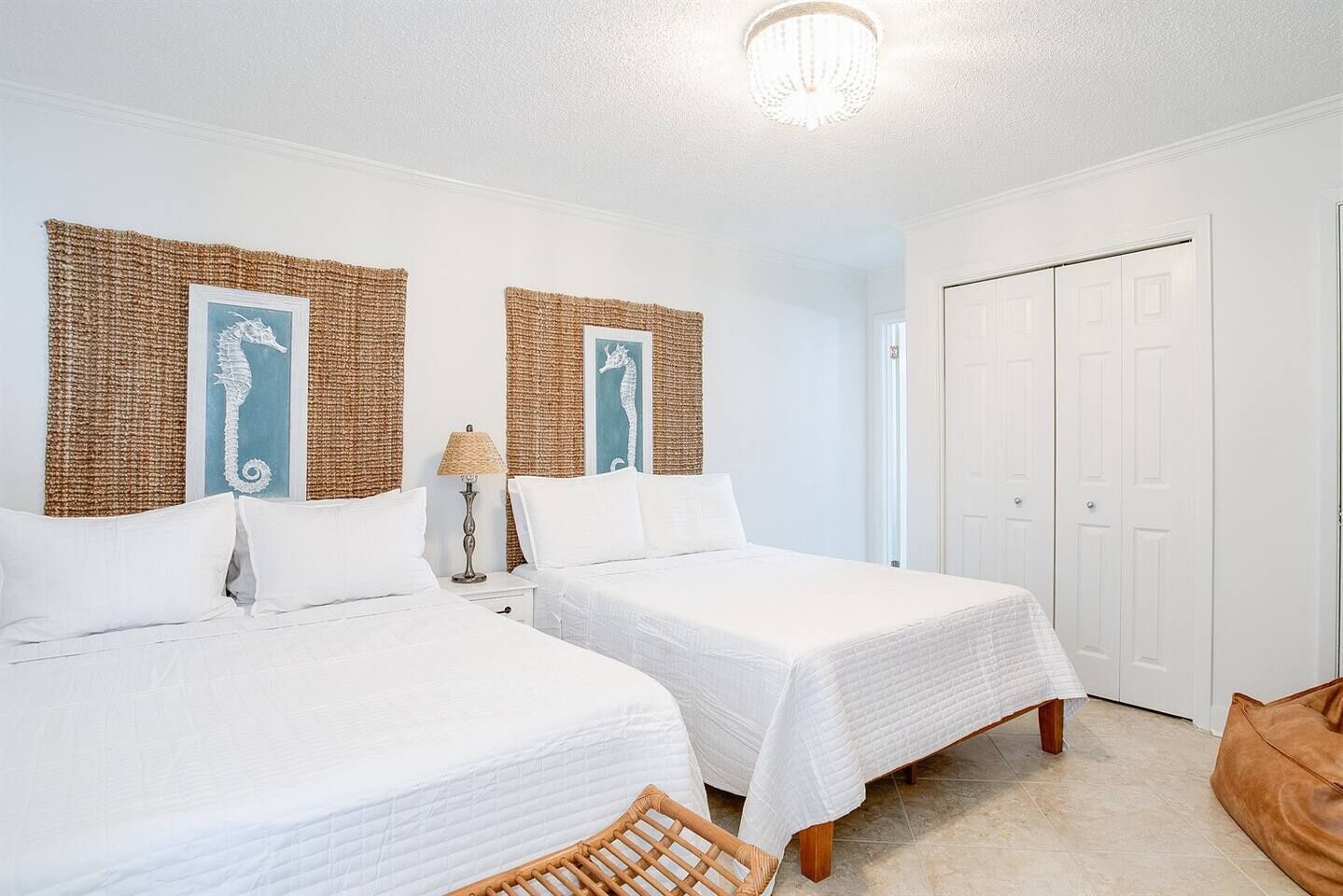 A hotel room with two beds, a wicker headboard, a lamp, a door, and a brown chair.