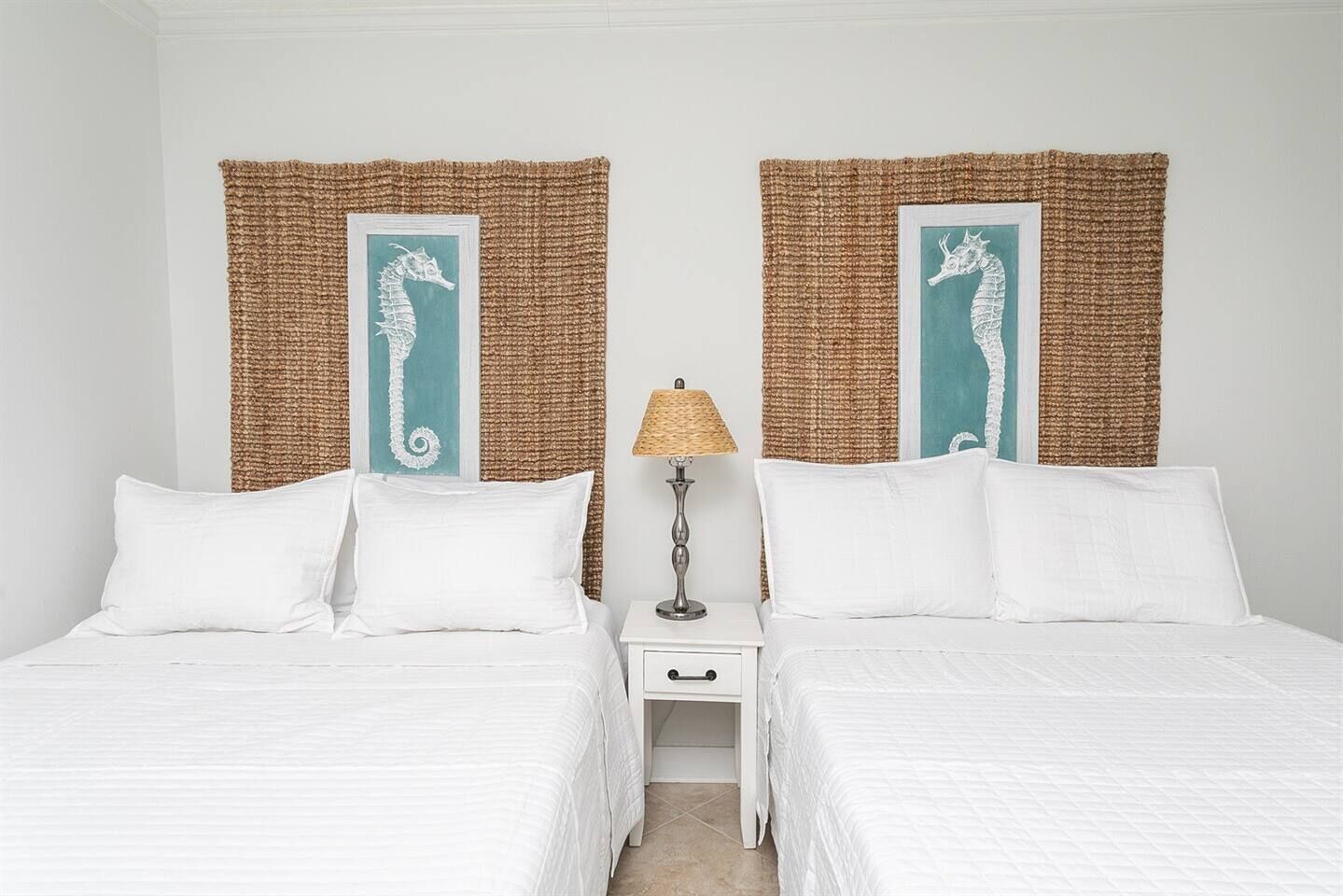 Een tweepersoonskamer met twee bedden, een nachtkastje met een lamp, en twee decoraties van zeepaardjes aan de muur.