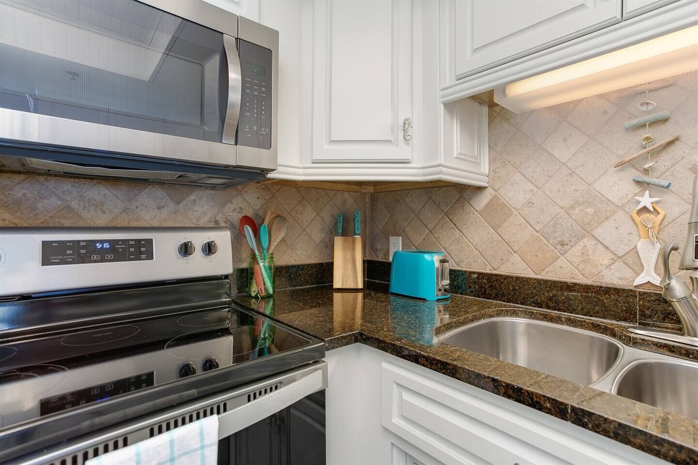 A modern kitchen with stainless steel appliances, a granite countertop, and white cabinetry.