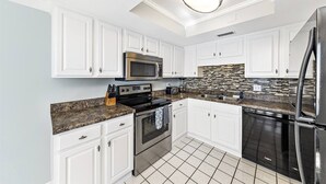 A modern kitchen with white cabinets, stainless steel appliances, a granite countertop, and a patterned backsplash.