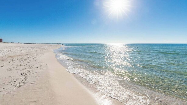 A beach with clear water, a sandy shore, and a bright sun.