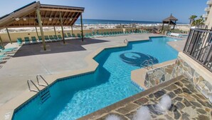 A swimming pool with a stone border, a wooden deck, and a view of the beach.