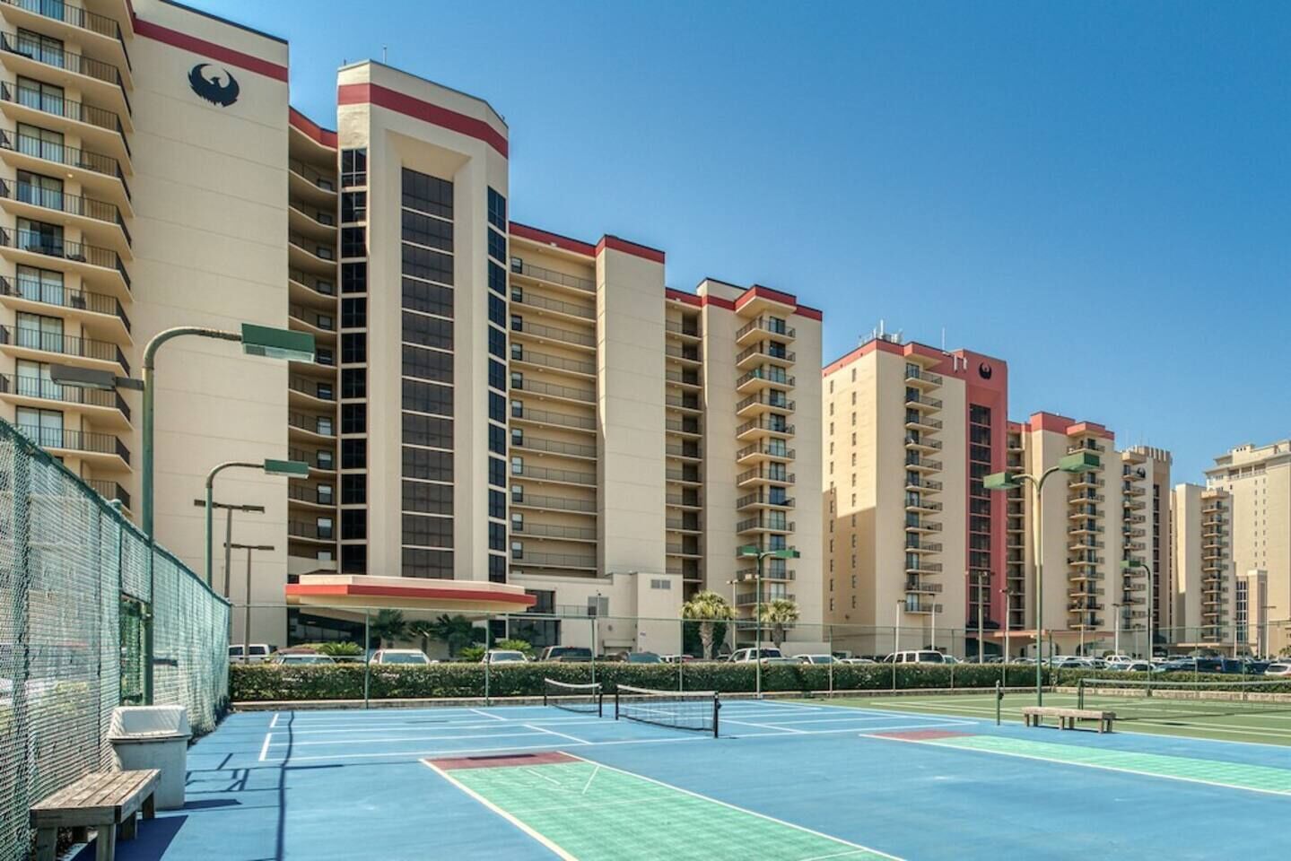 A multi-story hotel with balconies, a tennis court, and a parking area.