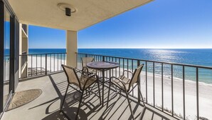 A balcony with a table and chairs, overlooking a beach and the ocean.