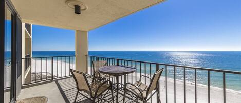 A balcony with a table and chairs, overlooking a beach and the ocean.