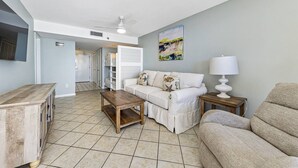 A living room with a white sofa, a wooden coffee table, a beige armchair, a white lamp, and a painting on the wall.