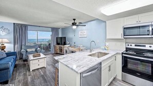 A modern kitchen with a built-in oven, a dining area with a view, and a living room with a blue sofa. - Plantation 6407-Beachfront Condo w/Heated Pool! (Gulf Shores)
