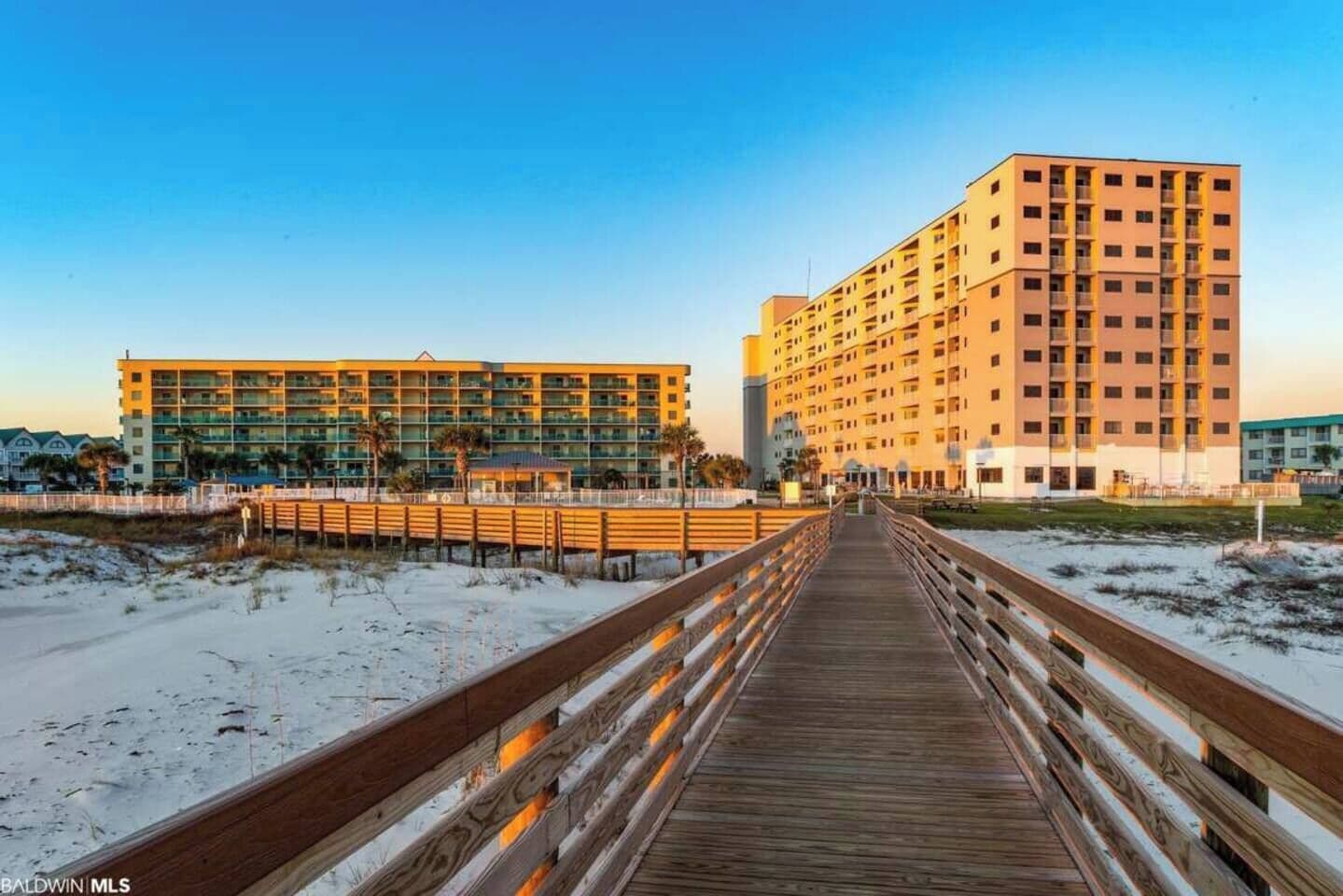 A wooden boardwalk leading to a hotel with multiple floors and balconies.