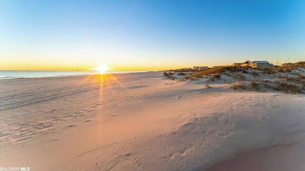 A beach with a sunset, sandy dunes, and a building in the background. - Plantation 6407-Beachfront Condo w/Heated Pool! (Gulf Shores)