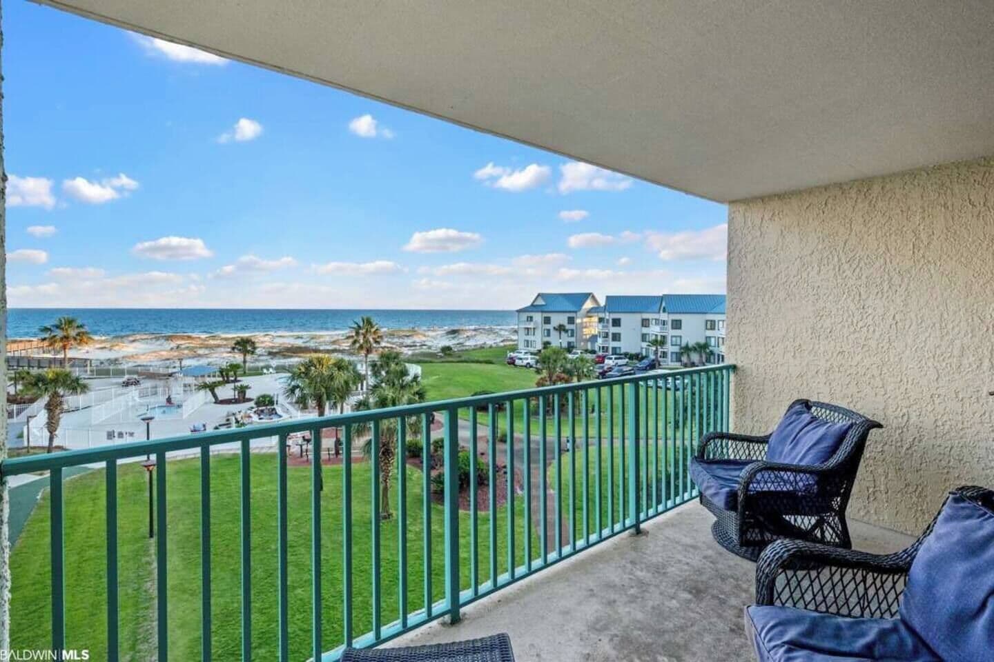 A balcony with a view of the beach, a pool, and a building with multiple windows.