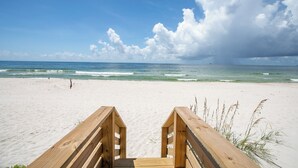 A wooden beach boardwalk leading to the ocean with clear skies and waves.