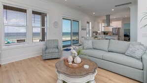 A spacious living room with a large grey sofa, a wooden coffee table with decorative items, and a view of the ocean through large windows.