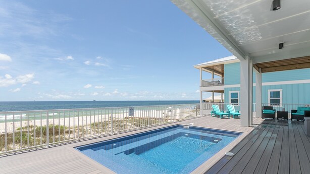 A pool on a wooden deck with a view of the beach and ocean.