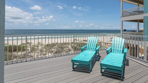 A balcony with two turquoise Adirondack chairs overlooking a beach.
