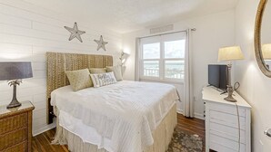 Un dormitorio con cama, mesita de noche, cómoda, espejo y ventana con vistas.