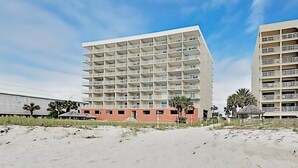 Un hotel de varios pisos con balcones, una playa en primer plano y palmeras.