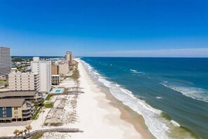 Un hotel frente al mar con vistas a la playa, varias construcciones y cielo despejado.