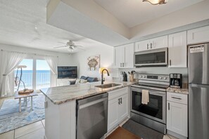 A modern kitchen with stainless steel appliances, a large island, and a view of the ocean. - Seacrest 803 - Coastal Charm | 1BR w/ Gulf & Lagoon Views + Pool Beach Front (Gulf Shores)