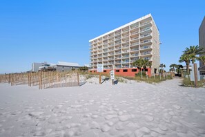 A beachfront hotel with multiple balconies, a sandy beach in the foreground, and a clear blue sky. - Seacrest 803 - Coastal Charm | 1BR w/ Gulf & Lagoon Views + Pool Beach Front (Gulf Shores)