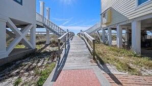 A wooden boardwalk leading to a white building with a balcony, under a clear sky.