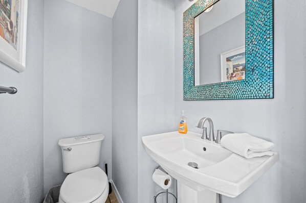 A bathroom with a white toilet, a sink with a mirror, and a roll of toilet paper.