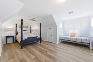 Une chambre à coucher avec un lit à baldaquin, un ventilateur de plafond, une fenêtre avec des volets et une petite table de chevet avec une lampe.