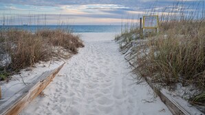 Ein Sandweg am Strand führt zum Meer, mit einem Schild, das Strandregeln anzeigt.