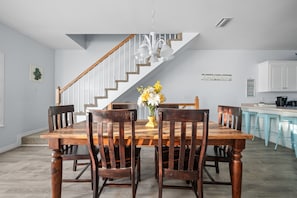 Ein Esszimmer mit Holztisch und -stühlen, einer Treppe und einer Küche mit hellblauen Barhocker.