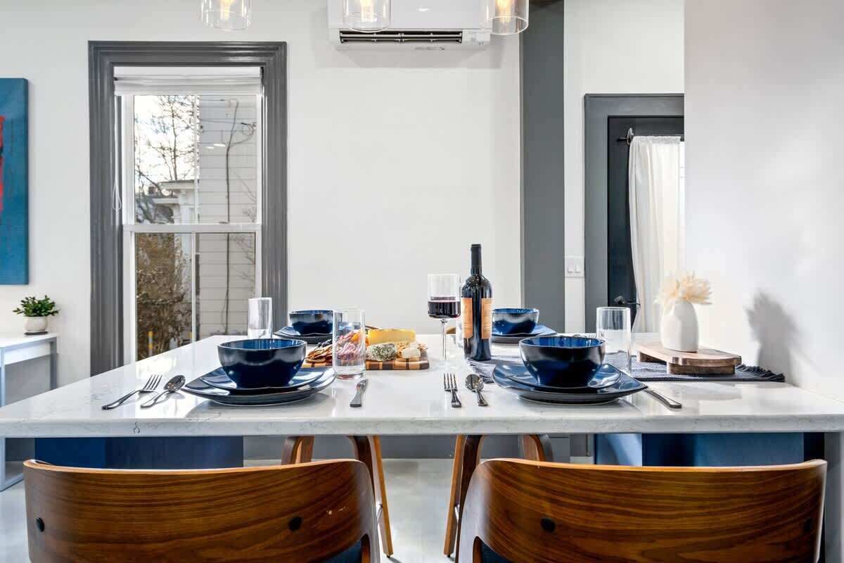 Een moderne eetruimte met een witte marmeren tafel, blauw servies en houten stoelen.
