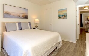 A neatly arranged bedroom with a large bed, a bedside table with a lamp, and two wall-mounted paintings. - Lani Kai Village 210, Great Rates & Beautiful Indirect Gulf Views from your unit (Gulf Shores)