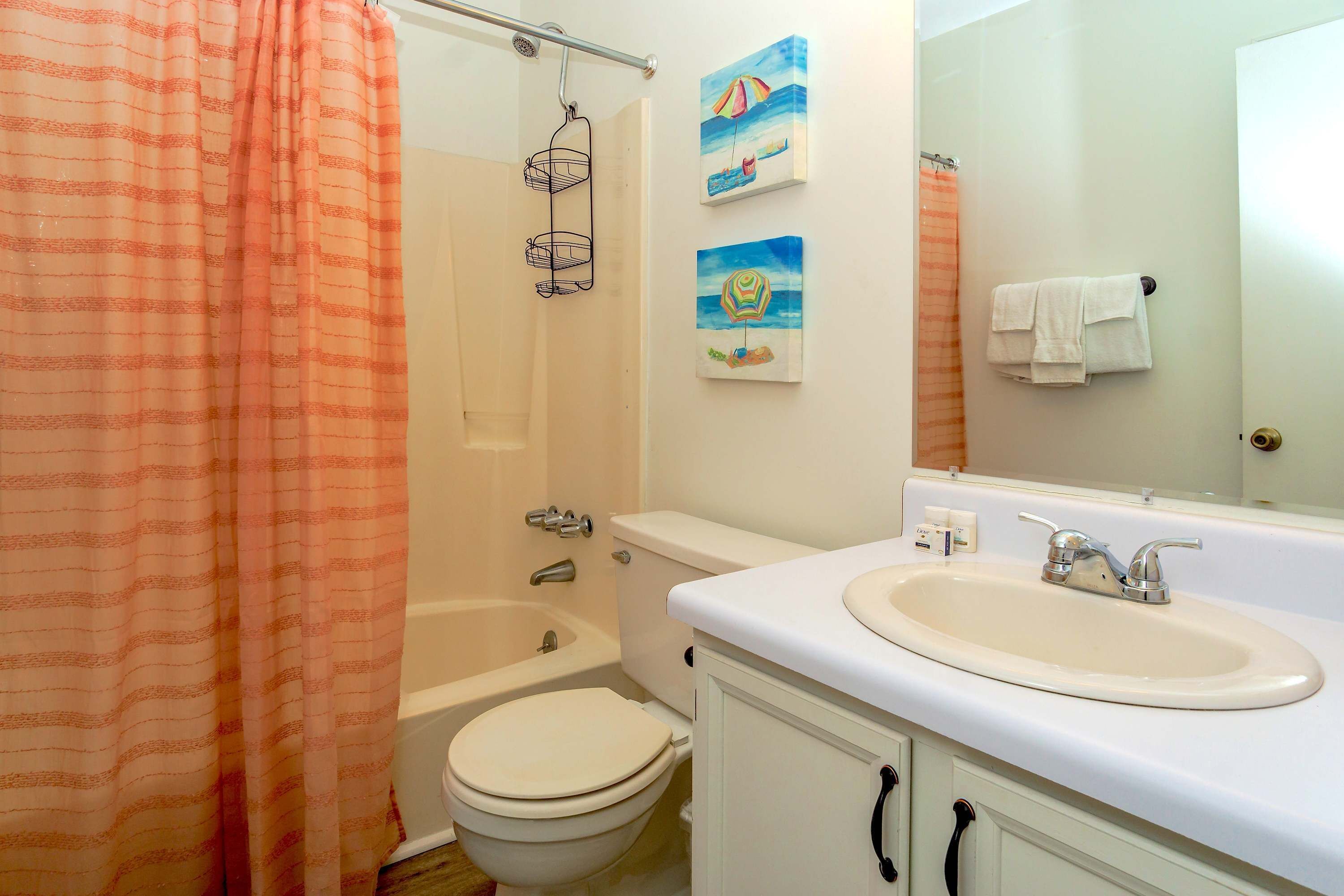Ein Badezimmer mit Badewanne, Toilette und Waschbecken. An der Wand befinden sich zwei Bilder und ein Handtuch hängt dort.