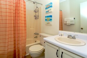 A bathroom with a bathtub, toilet, and sink. There are two paintings on the wall and a towel hanging on the wall.