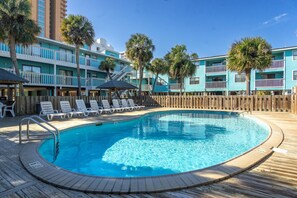 A swimming pool with a wooden deck, lounge chairs, and a wooden fence.