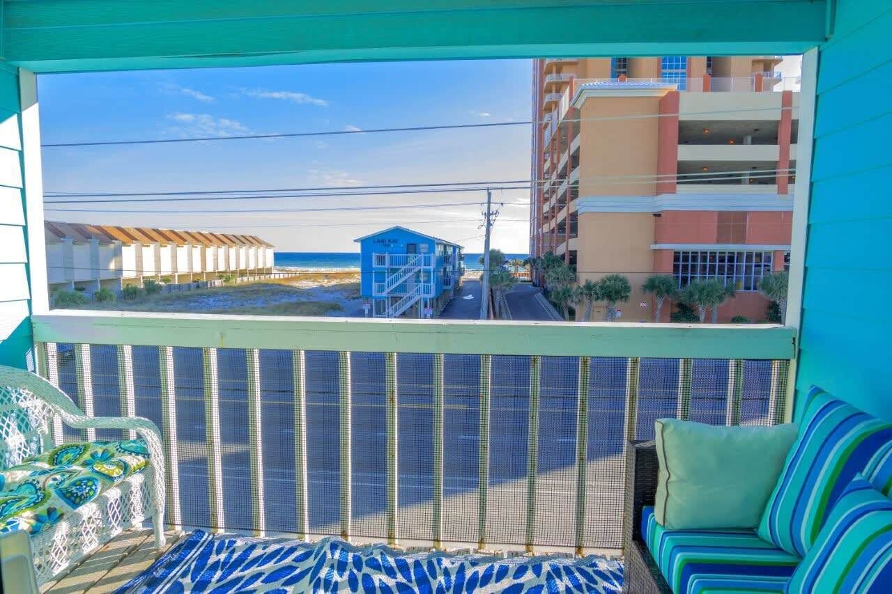 A balcony with a view of the beach, a blue building, and a multi-story hotel.