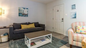 Ein Wohnzimmer mit grauem Sofa, einem Holztisch, einem gestreiften Sessel und einer Tür.