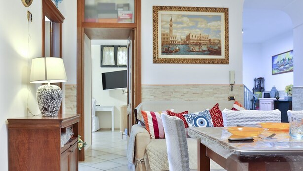 A living room with a sofa, a coffee table, a TV, and a framed painting of a cityscape. - GuestHost - Cozy apartment that can accommodate up to 6 people, located in an independent villa with garden. The apartment is 900 meters from the Circumvesuviana for Naples-Pompei-Sorrento, perfect for traveling in the area and reaching all points of int (San Giorgio a Cremano)