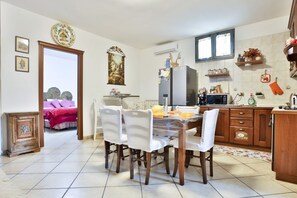 A dining area with a wooden table and chairs, a kitchen with a refrigerator and microwave, and a bedroom with a bed and a door leading to another room.