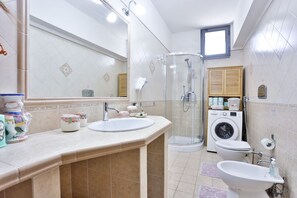 A bathroom with two sinks, a shower, a washing machine, and a toilet.