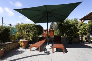 A patio with two wooden lounge chairs, a table, and a large umbrella.