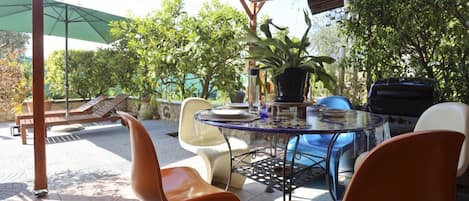 An outdoor patio with a round table, chairs, a grill, and potted plants.