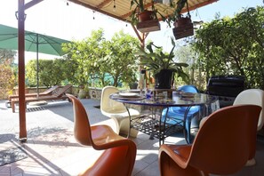 An outdoor patio with a round table, chairs, a grill, and potted plants.
